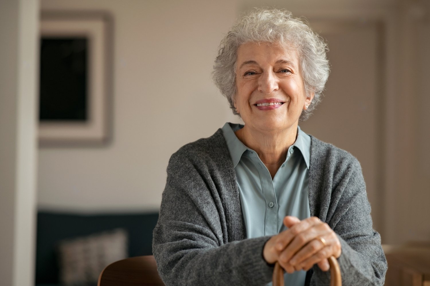 portrait-of-smiling-mature-woman-holding-walking-stick-and-sitting-on-chair-at-home-portrait-of-1926782000-transformed